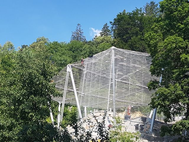 Eine große Metallstruktur ist von Bäumen und einem blauen Himmel umgeben.