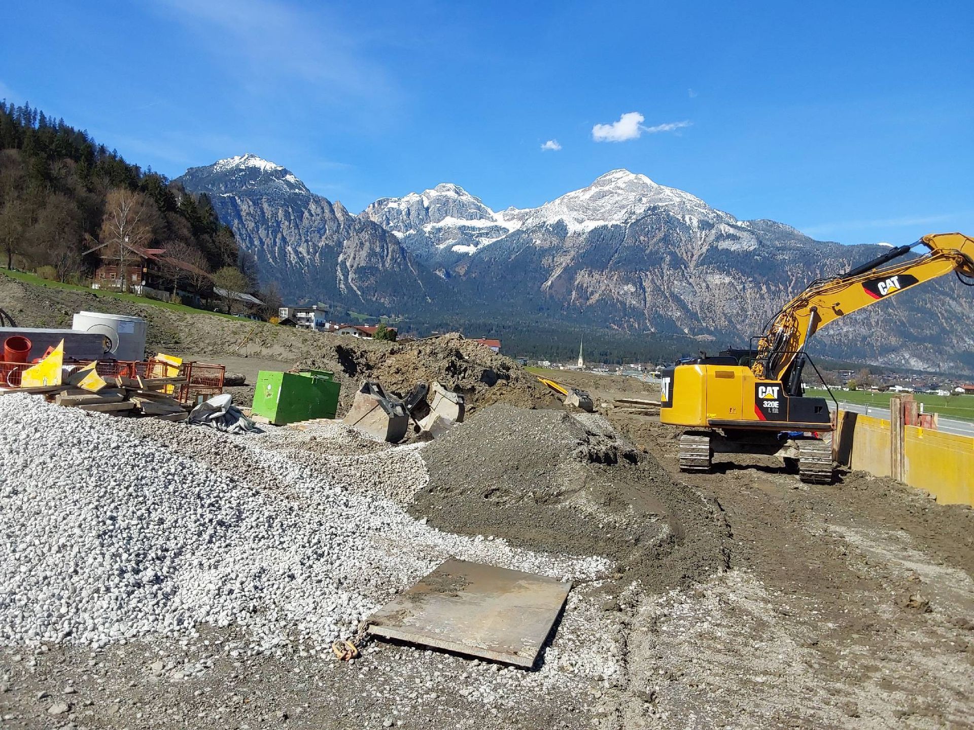 Ein großer gelber Bagger arbeitet auf einer Baustelle mit Bergen im Hintergrund.