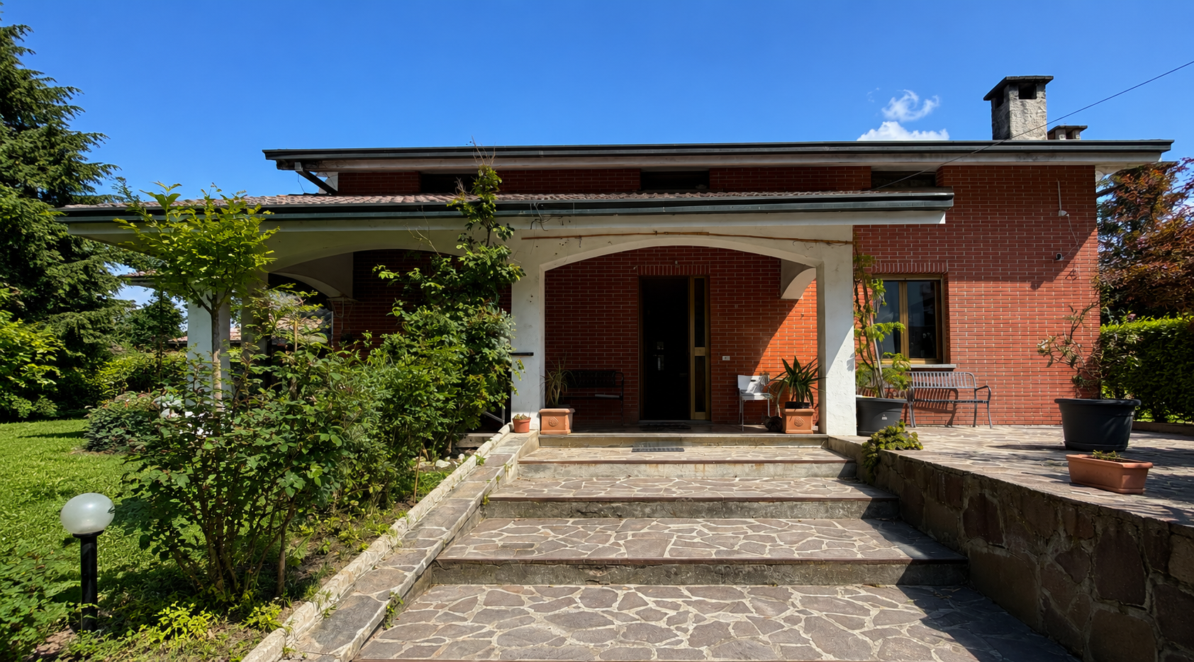 Balcone in mattoni con sedie e ringhiera in metallo nero, affacciato su una verde collina e con area salotto esterna.