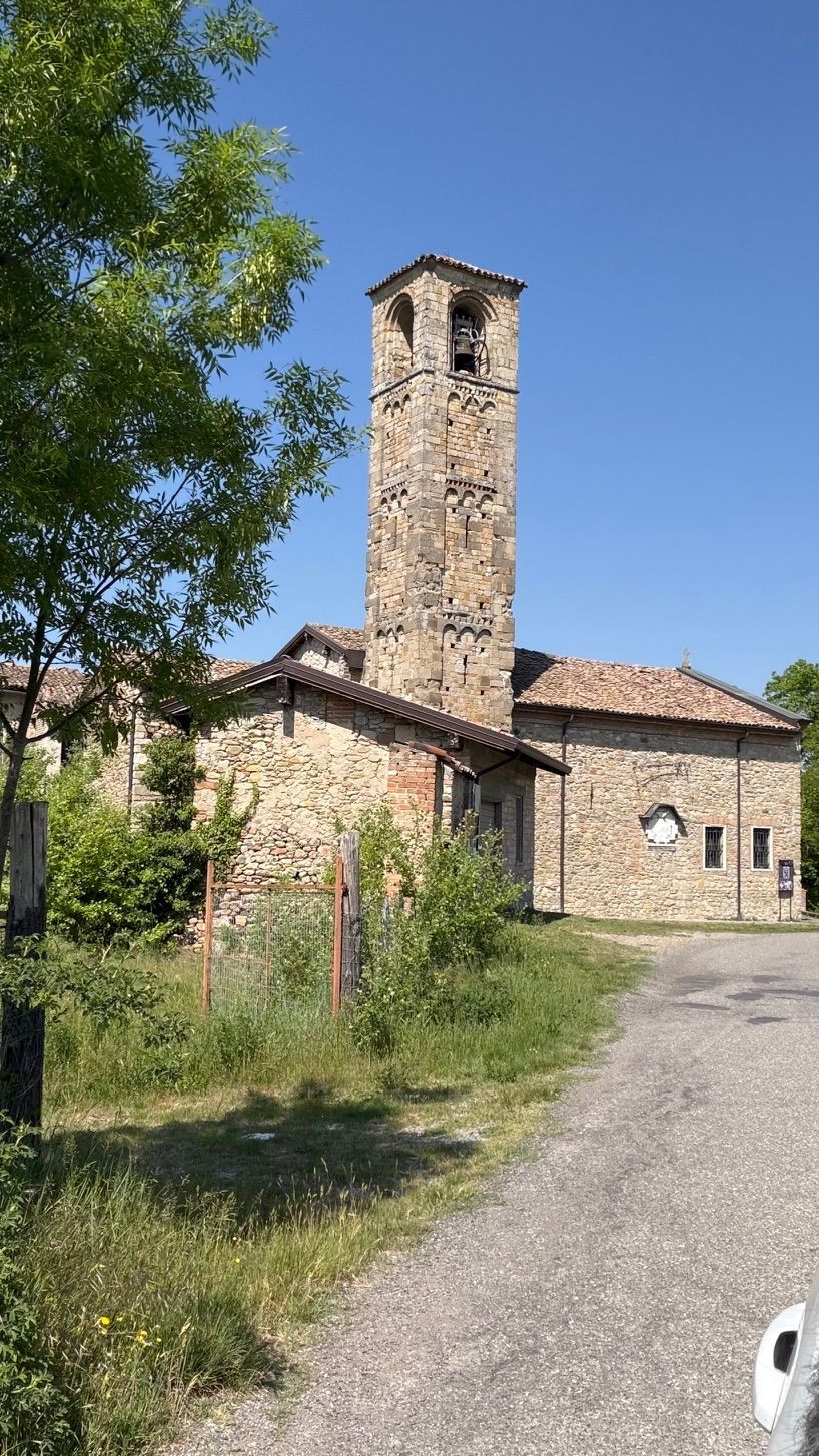 Chiesa in pietra con un alto campanile accanto a un sentiero di ghiaia sotto un cielo azzurro e limpido.