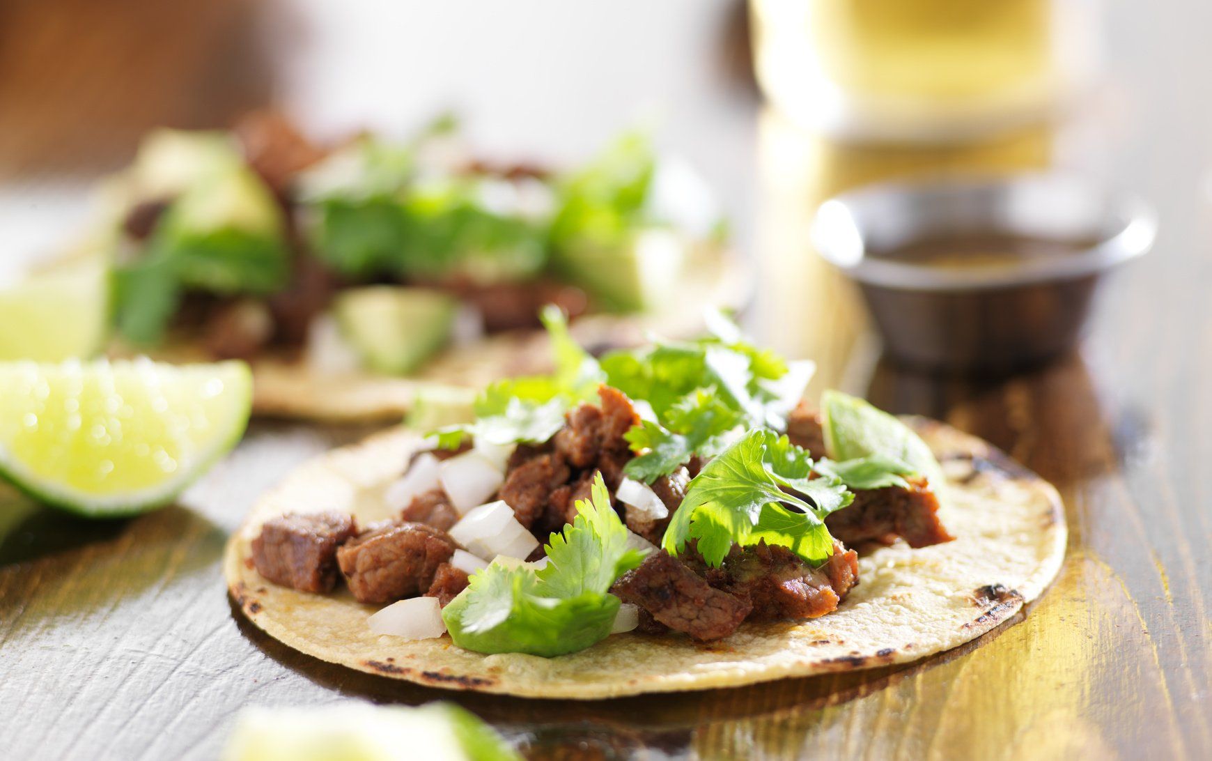 Tacos with steak, onions, cilantro, and lime on a wooden table.