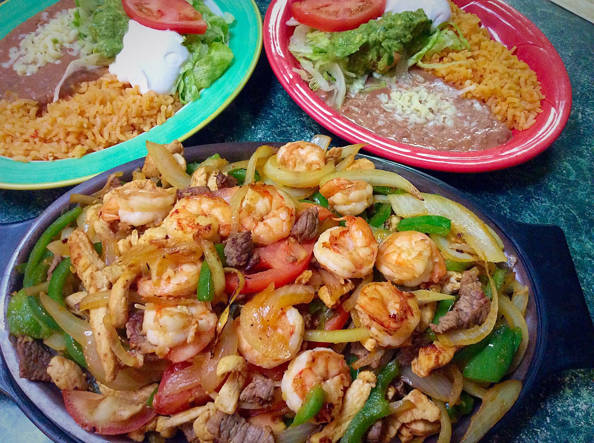 Sizzling fajitas with shrimp, steak, and chicken, with sides of rice, beans, and salad.