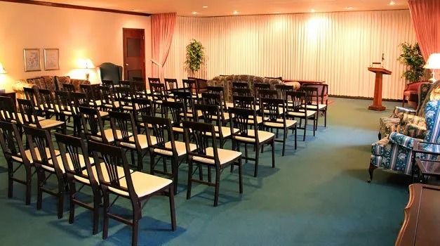 A viewing room with rows of chairs, stage, and curtains. Green carpet.