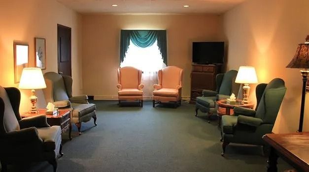 A viewing room with green and tan chairs, lamps, and a window.