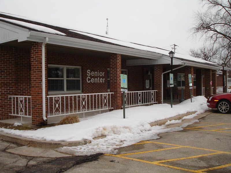 A red car is parked in front of a building that says senior center