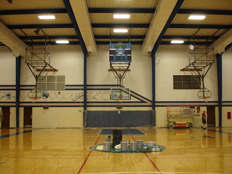 An empty gym with a basketball hoop and a scoreboard