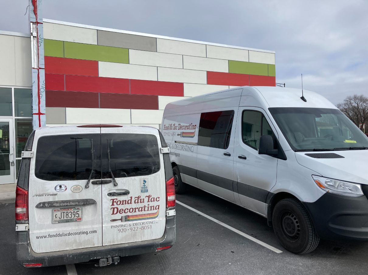 Two white vans are parked in a parking lot in front of a building.