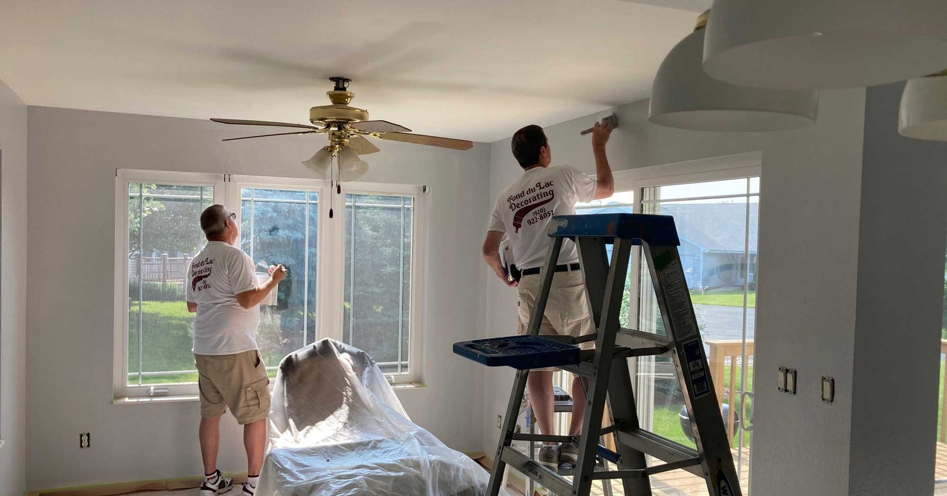 Two men are painting the ceiling of a living room.