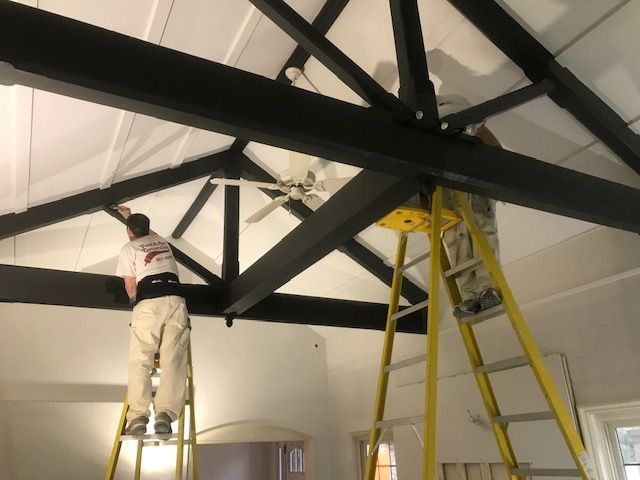 A man standing on a ladder painting a ceiling