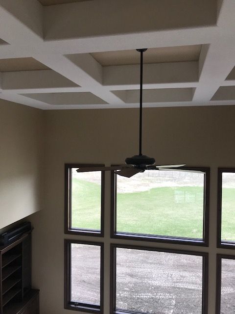 A ceiling fan hangs from the ceiling of a room with lots of windows