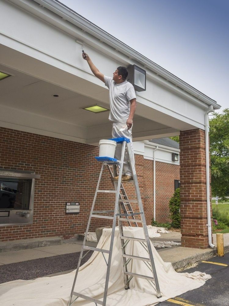 Person on A Ladder Painting the White Overhang of A Brick Building — A1 Painting NQ in Mareeba, QLD