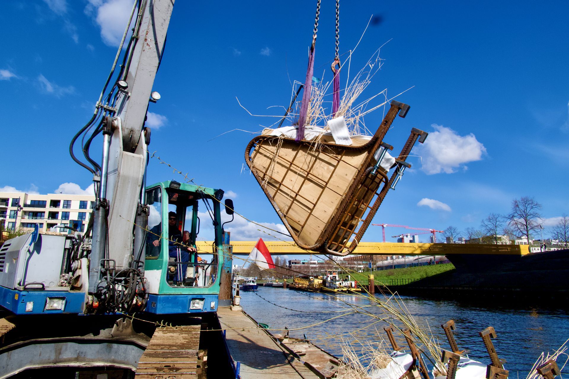 Ein bepflanztes Modul  der Vertical Wetlands schwebt aufgehängt an einem Kran vom Ufer auf ein Schiff zur Installation. 