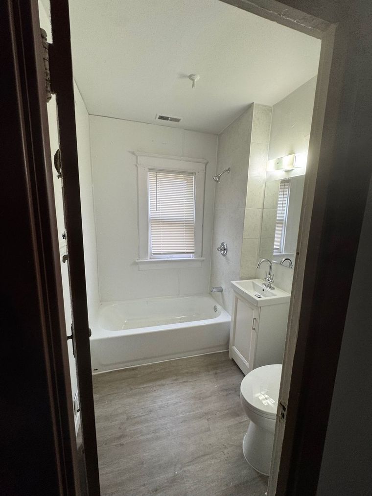 A bathroom with a tub , sink , toilet and window.