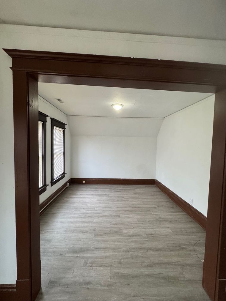 An empty living room with hardwood floors and white walls.