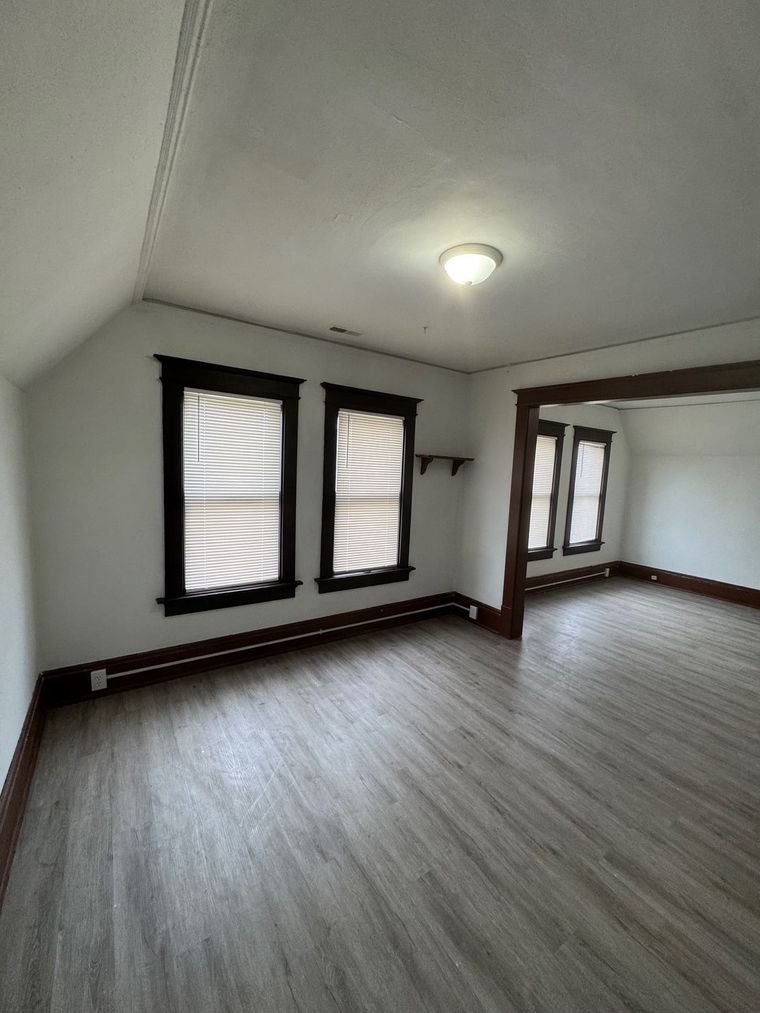 An empty living room with hardwood floors and two windows.