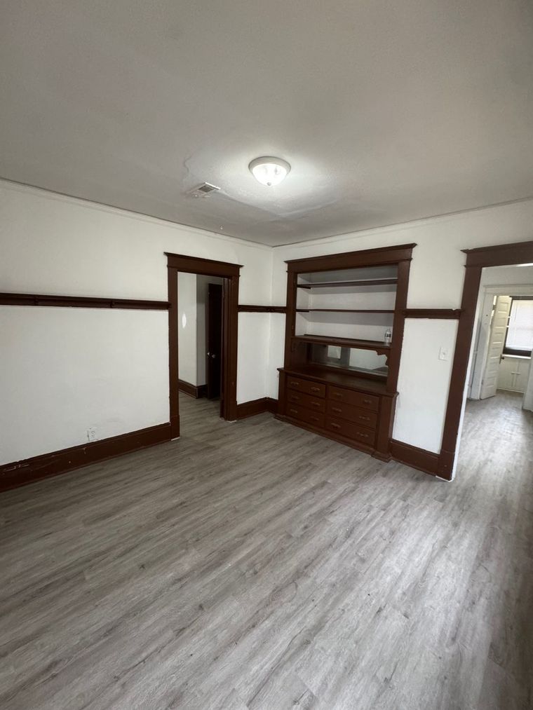 An empty living room with hardwood floors and white walls.