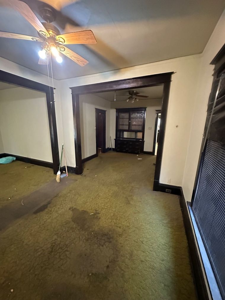 An empty living room with a ceiling fan and a window.