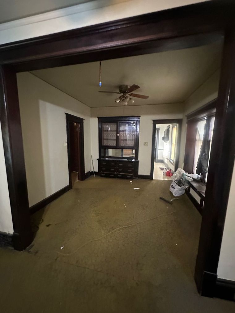 An empty living room with a ceiling fan and a dresser.