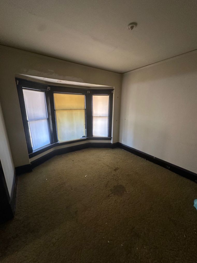 An empty room with a large window and a carpeted floor.