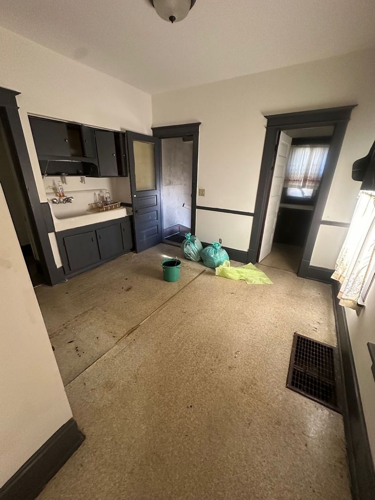 An empty kitchen with a sink and a bucket on the floor.