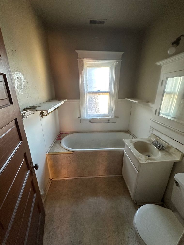 A bathroom with a tub , sink , toilet and window.