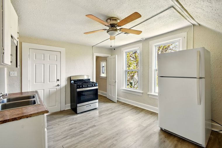 A kitchen with a stove , refrigerator , sink and ceiling fan.