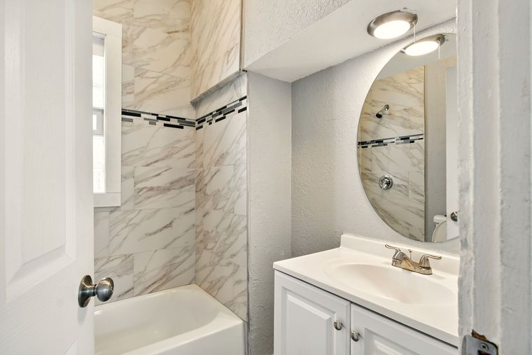 A bathroom with a sink , tub and mirror.