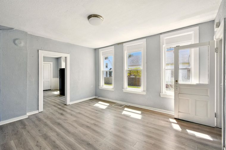 An empty living room with hardwood floors and three windows.