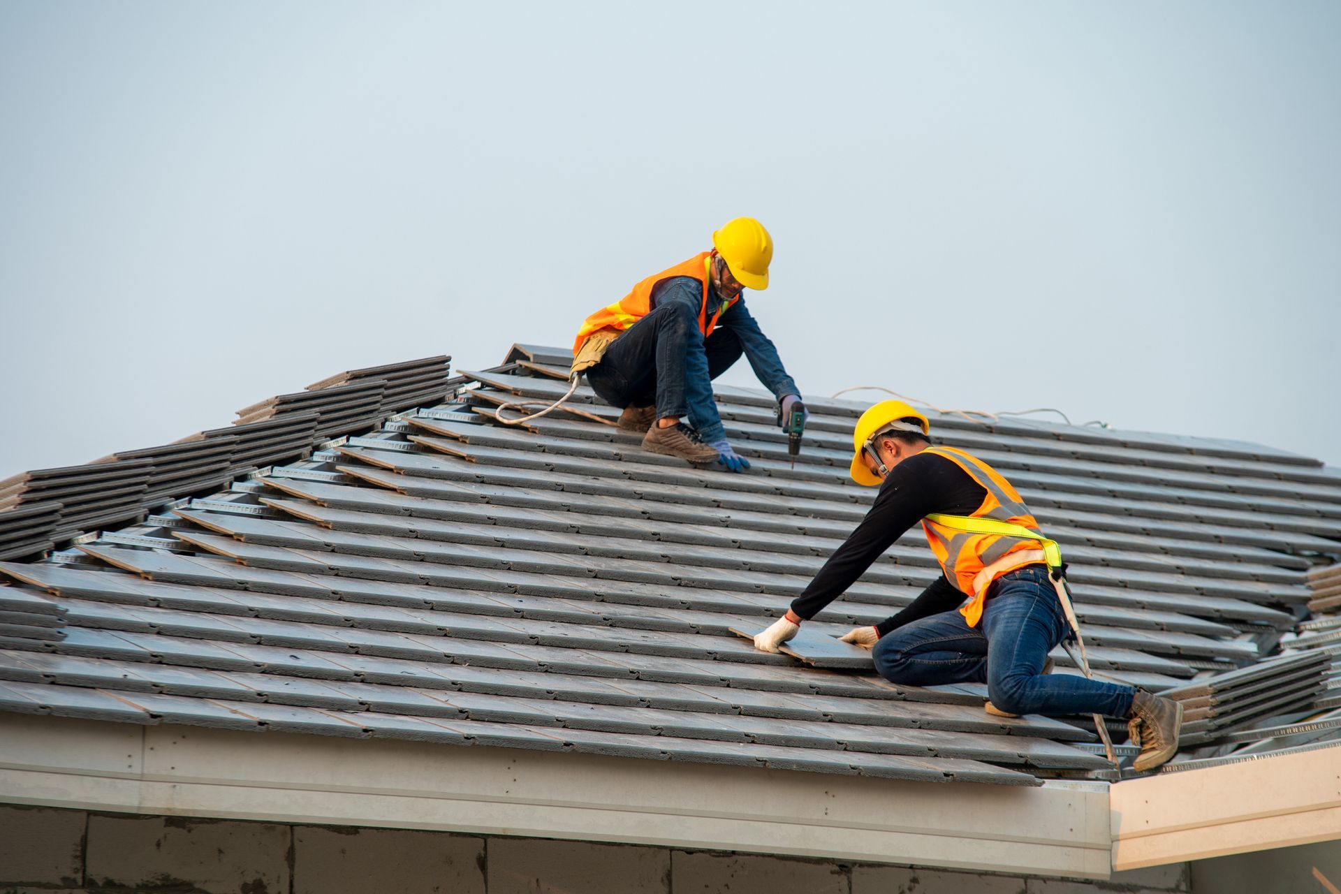 Workers in yellow helmets installing tiles on a sloped roof, residential roofing in progress.