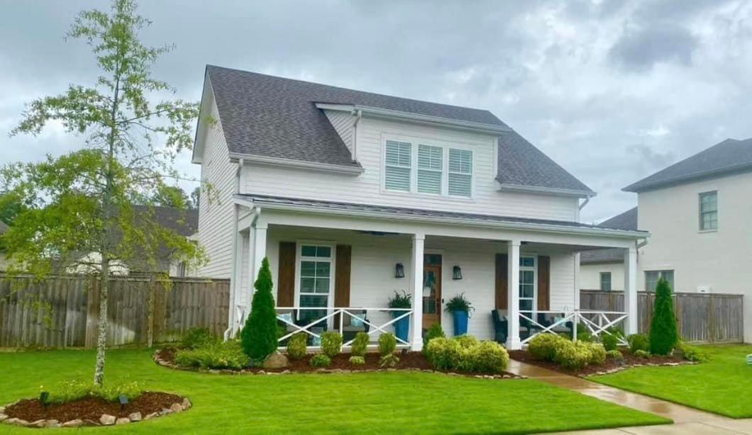 A white house with a porch and a tree in front of it.