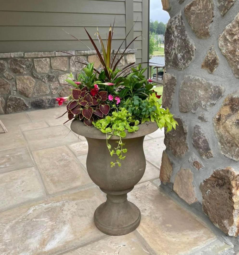 A large vase filled with flowers and plants is sitting on a tiled floor.