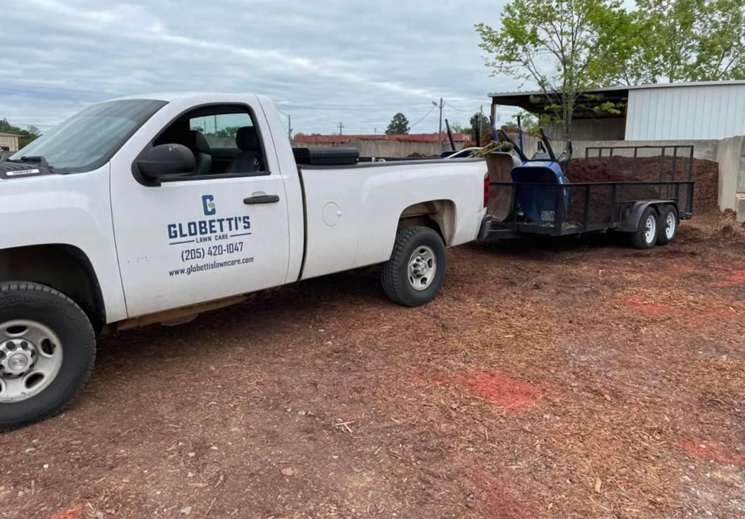 A white truck with a trailer attached to it is parked in a dirt lot.