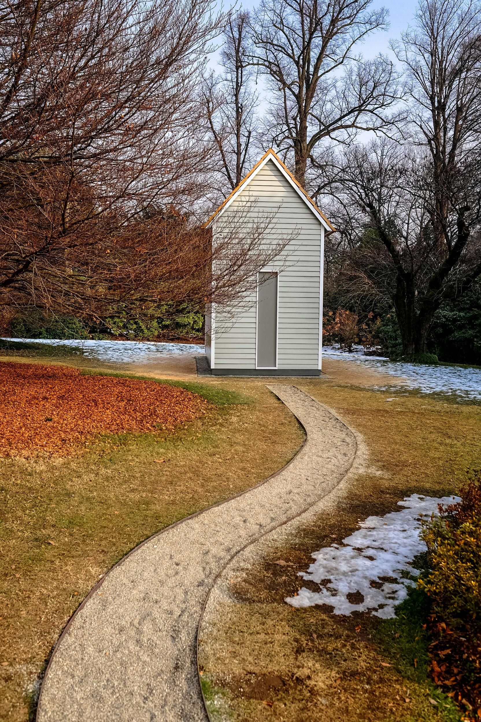 A path leading to a small white house in the middle of a park.