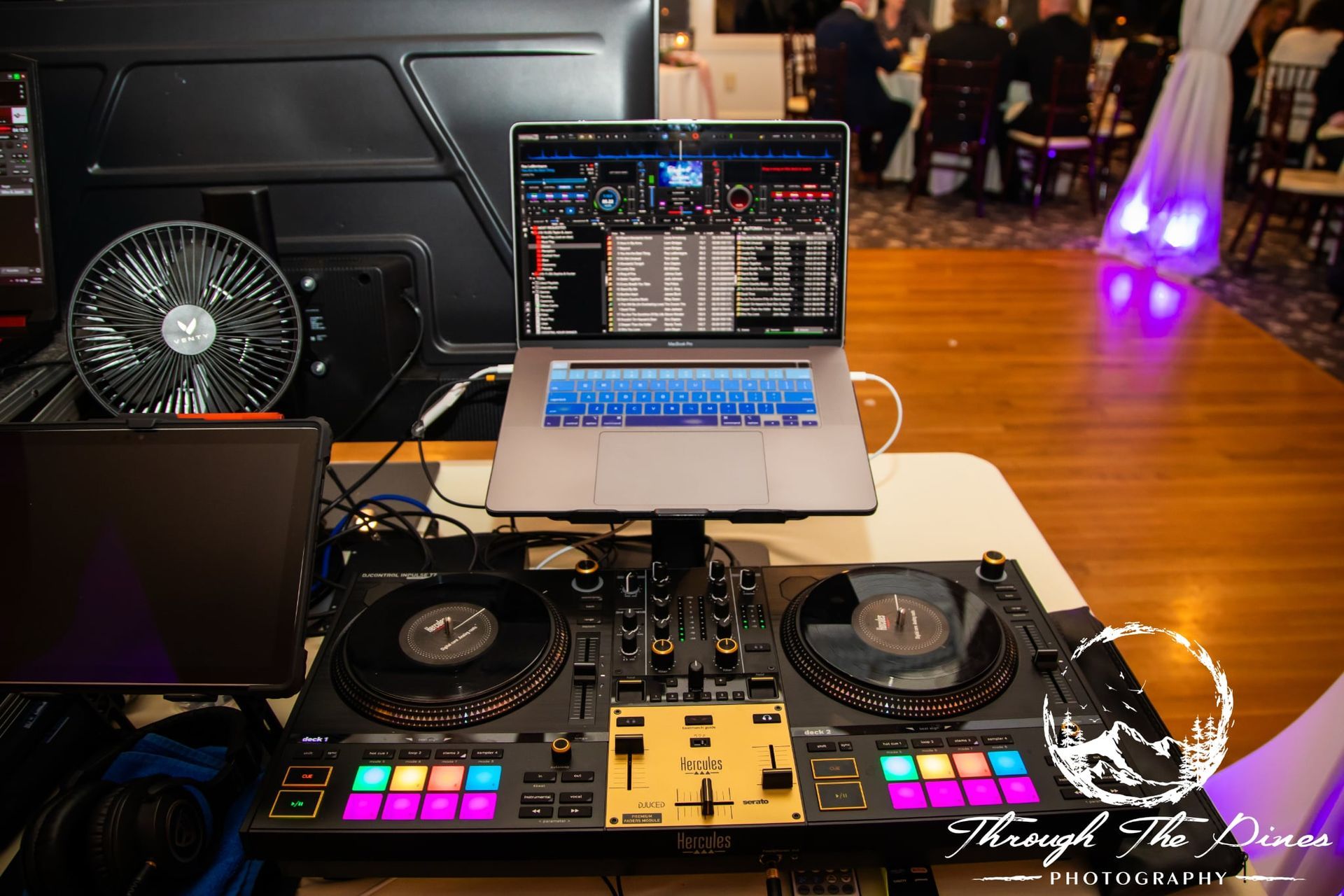 DJ setup with laptop and mixer on a table in a room with a dance floor.