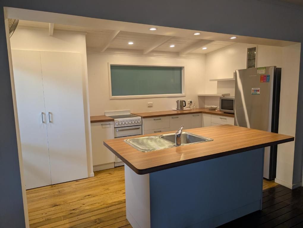 A brightly lit kitchen with a central blue island, wooden countertops, white cabinets, and a stainless steel refrigerator.