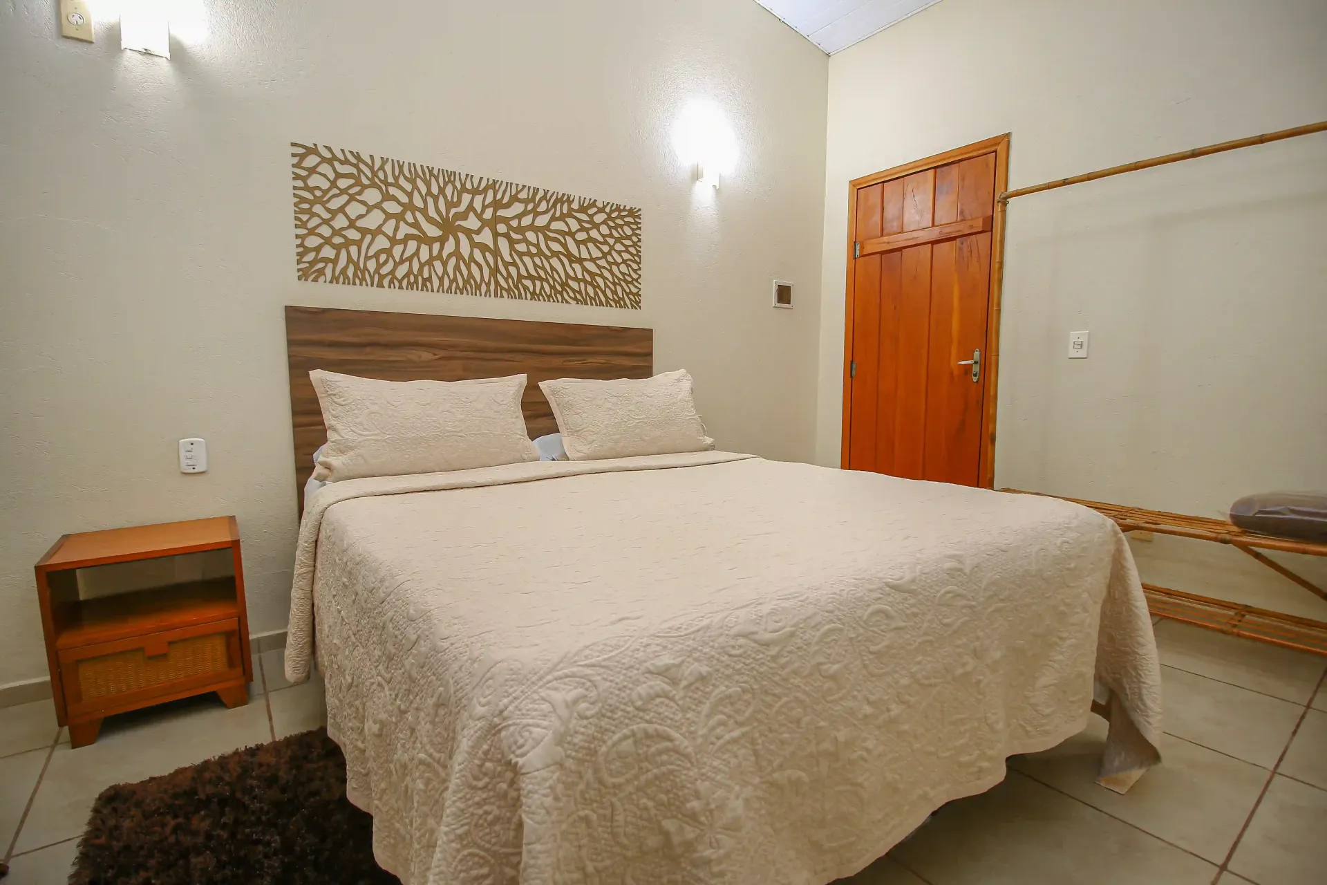 Um quarto com uma cama, mesa de cabeceira e porta - Pousada Flores do Cerrado