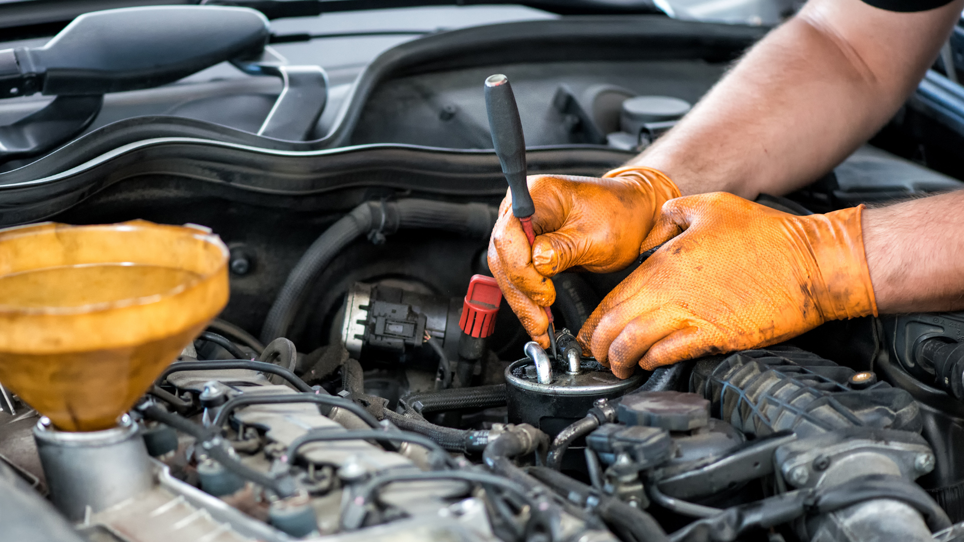 A man wearing orange gloves is working on the engine of a car.