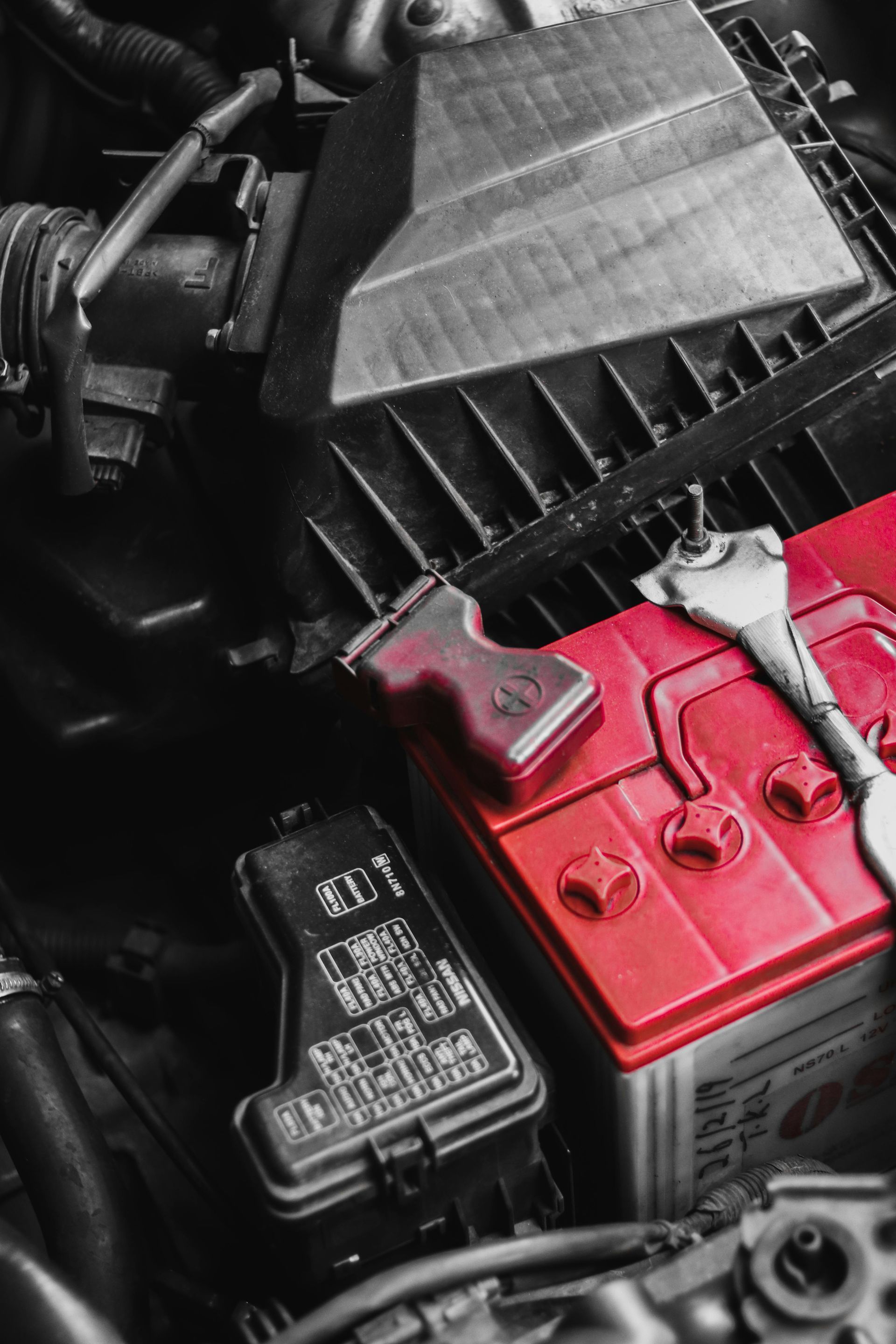 A red battery is sitting under the hood of a car.
