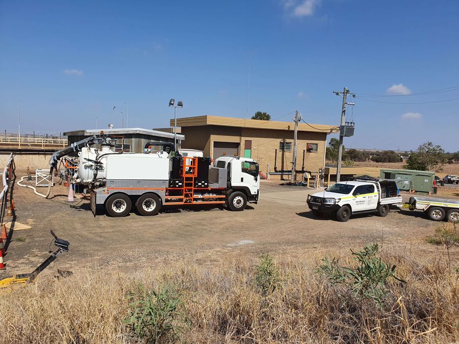 A vacuum truck is parked in a field in front of a building.