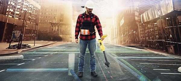 A man is standing on a city street holding a metal detector.