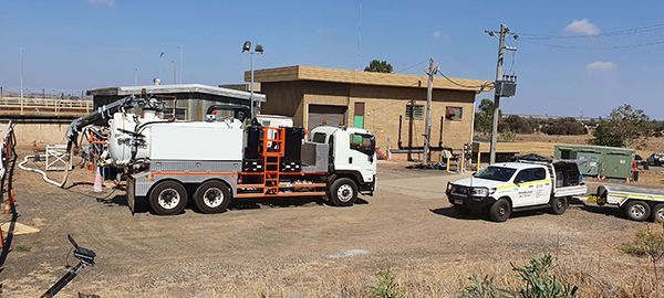 A vacuum truck is parked in a field in front of a building.