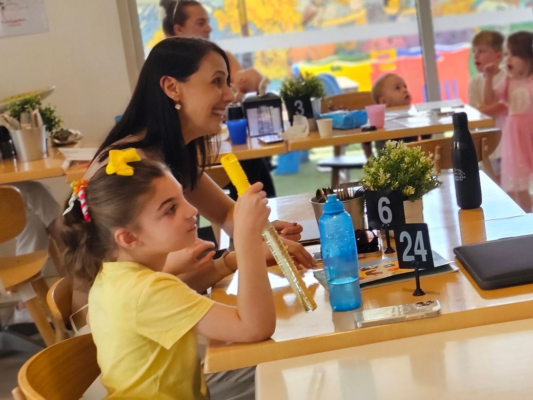 A little girl in a yellow shirt is sitting at a table with a number 6 on it