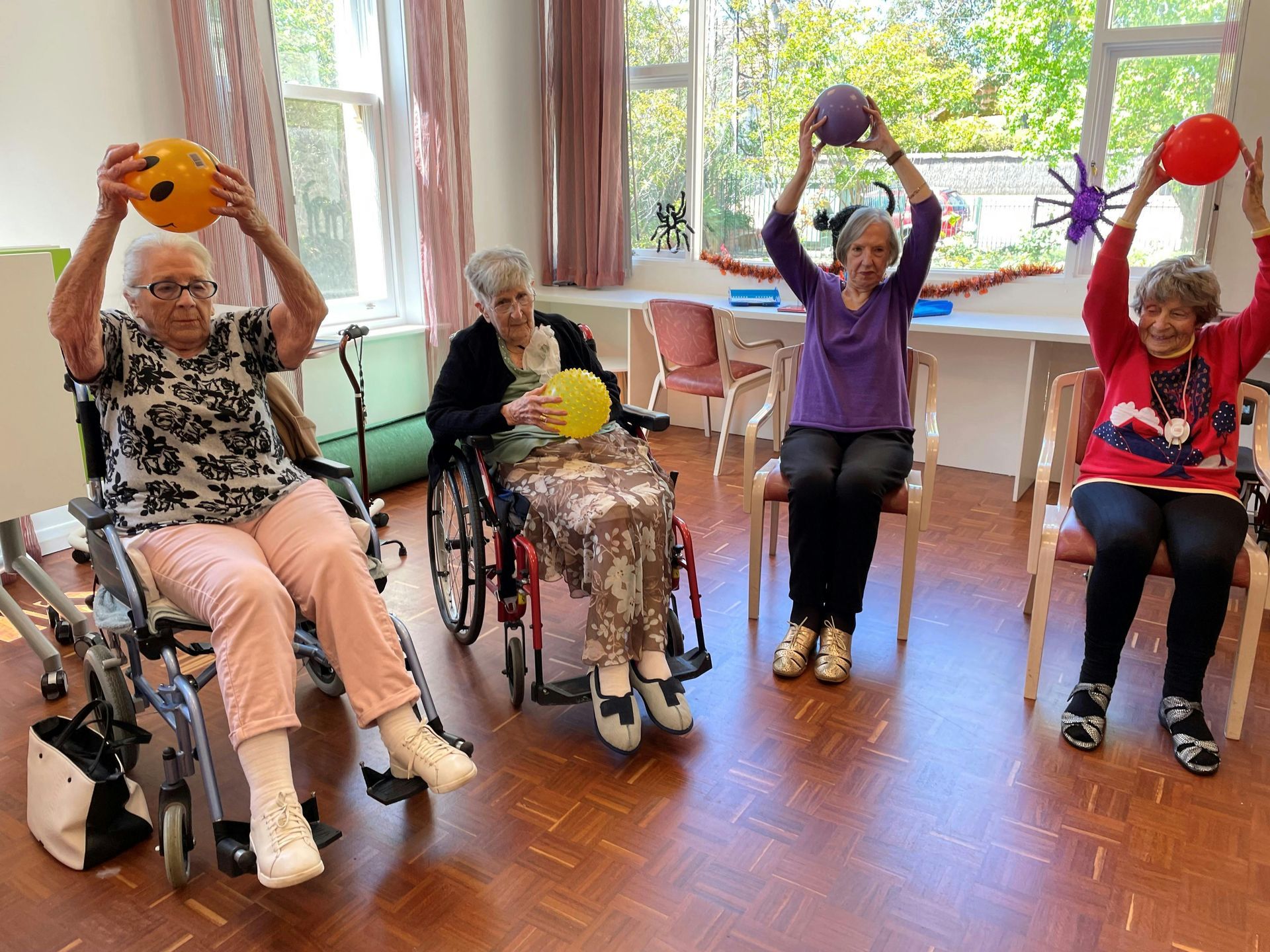 A group of elderly women in wheelchairs are doing exercises with balls.