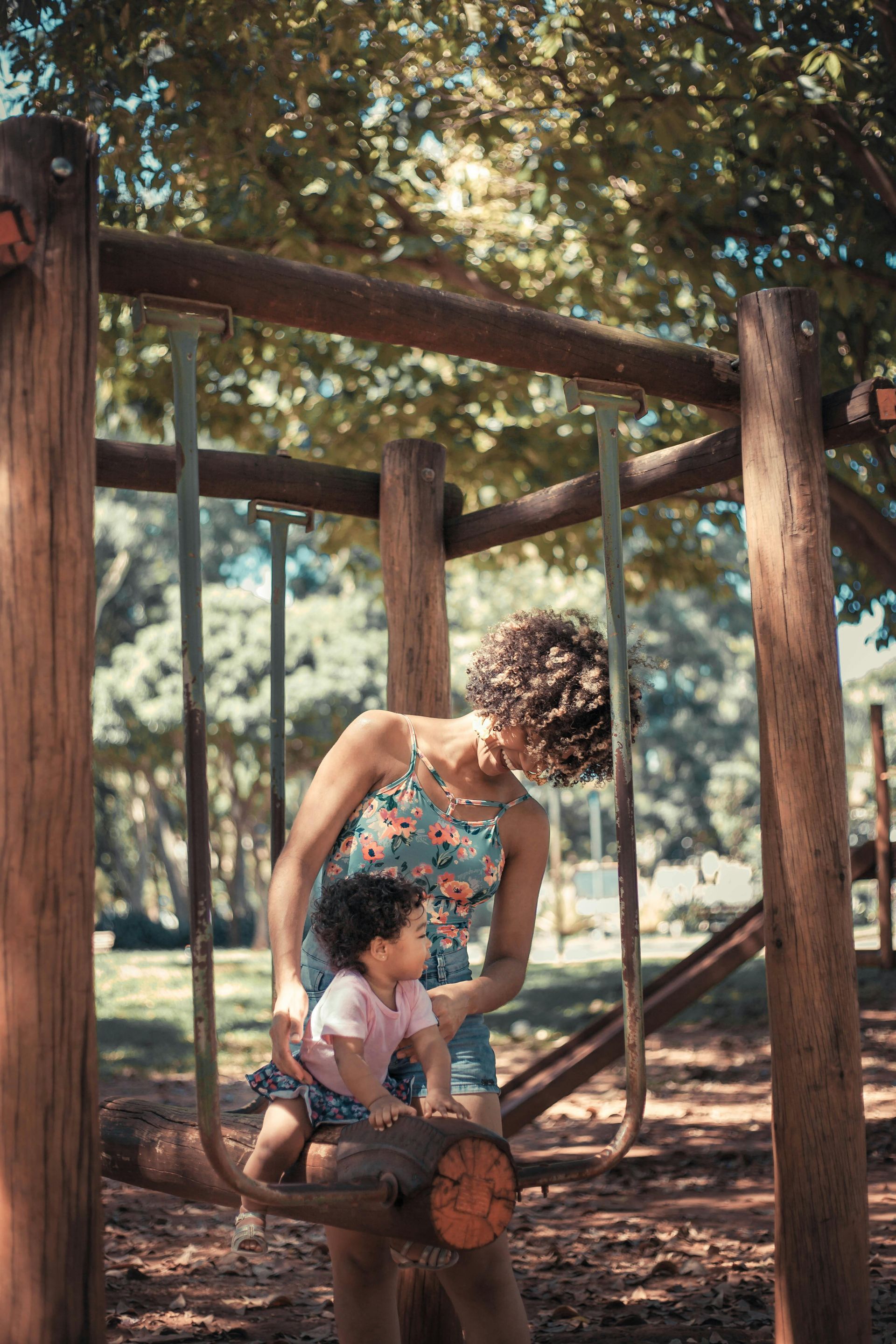 A woman and a child are playing on a swing set in a park.