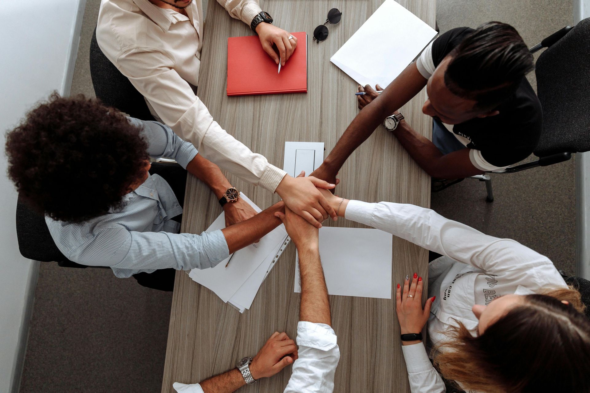 Colleagues stacking hands over a table with papers, meeting in progress from overhead view