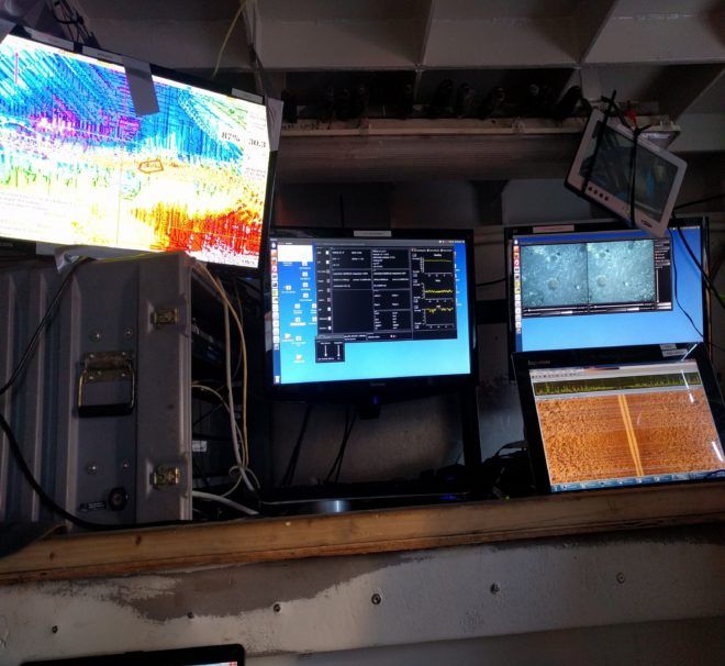 A row of computer monitors are lined up on a wooden shelf
