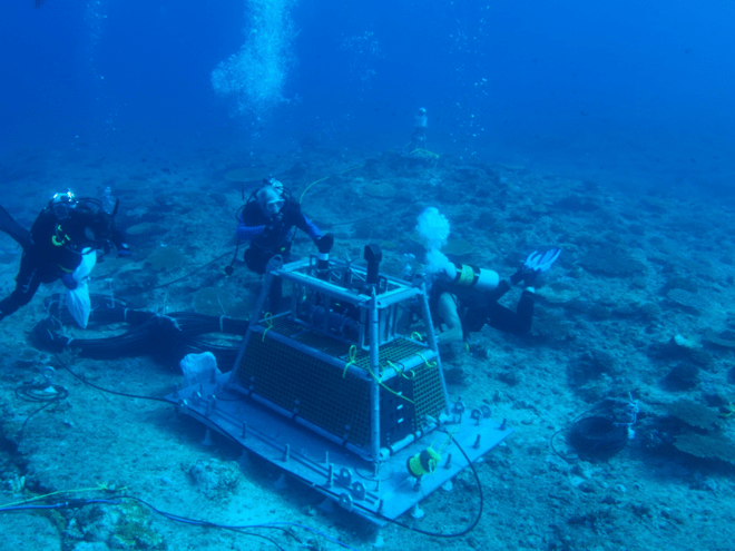 A group of scuba divers are working on a machine in the ocean.