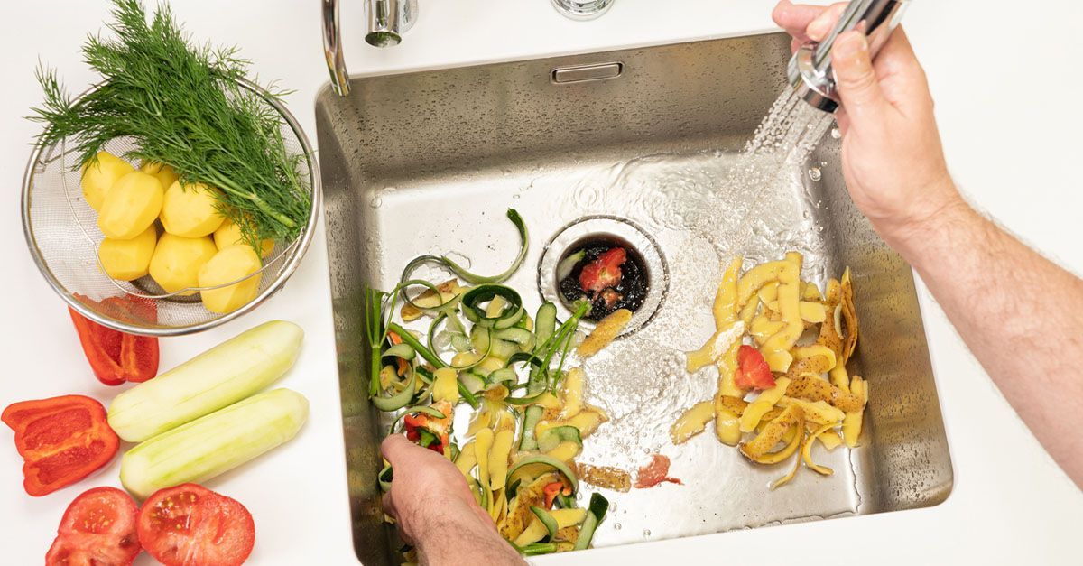 A kitchen sink being used to put vegetable scraps into the disposal.