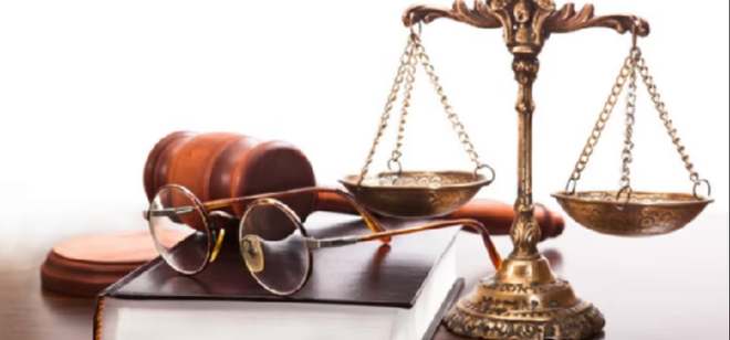 Un mazo de juez, una balanza de justicia, unas gafas y un libro sobre una mesa.