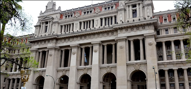 Un gran edificio con columnas y arcos está rodeado de árboles.